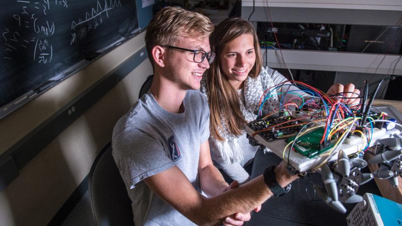 Two engineering students holding up a robot